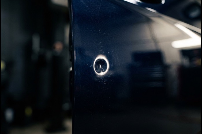 Small round door ding on a navy car door under raking light